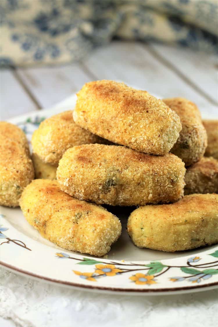 flowery white plate piled with potato croquettes on wood board