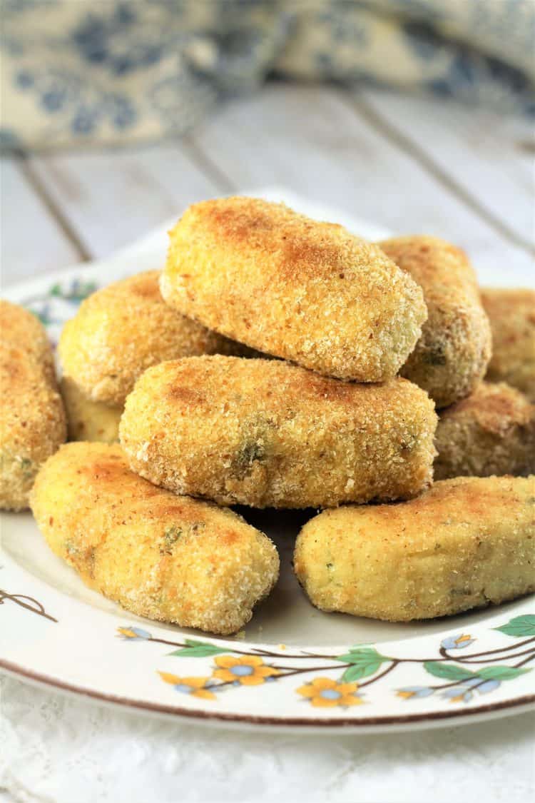 flowery plate piled with potato croquettes on wood board