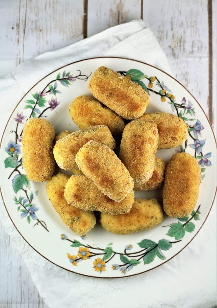 large flowery plate piled with potato croquettes on white dish towel 