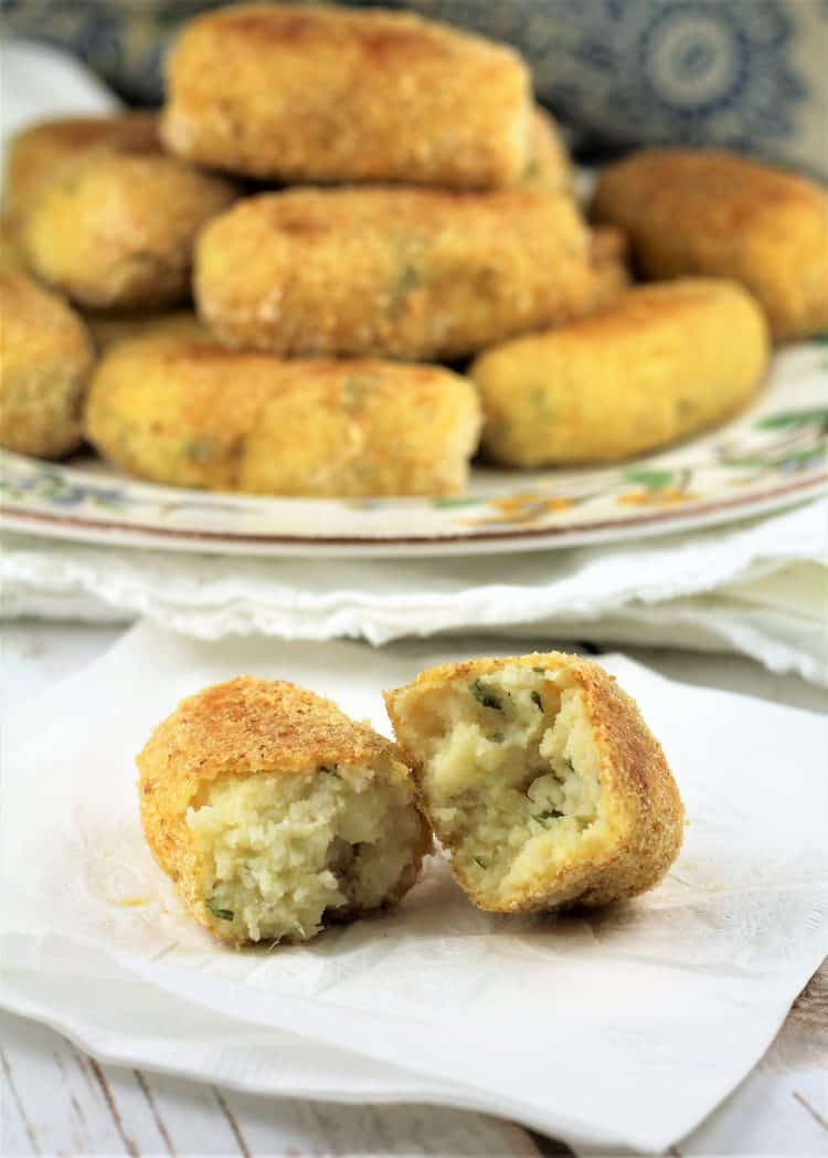 potato croquette cut in half to reveal interior with plate of croquettes in background