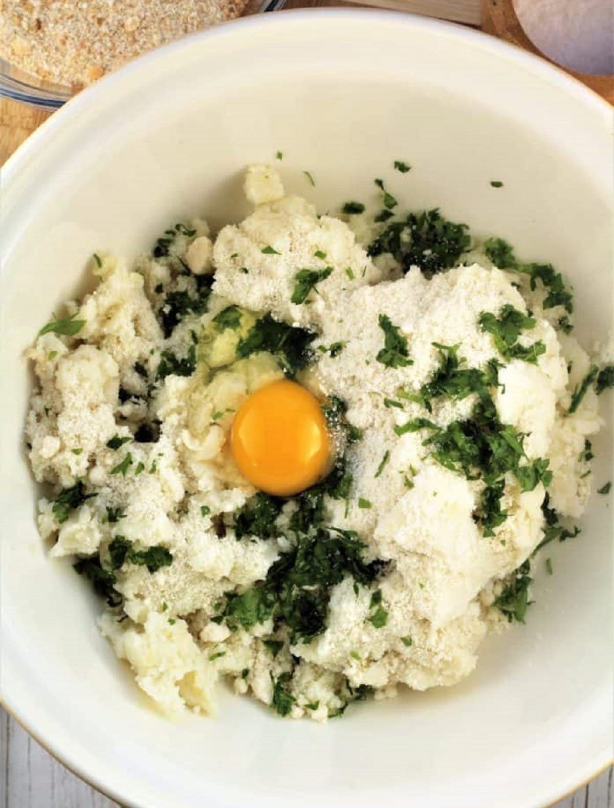 Bowl with mashed potatoes, cheese, parsley and egg for croquettes.