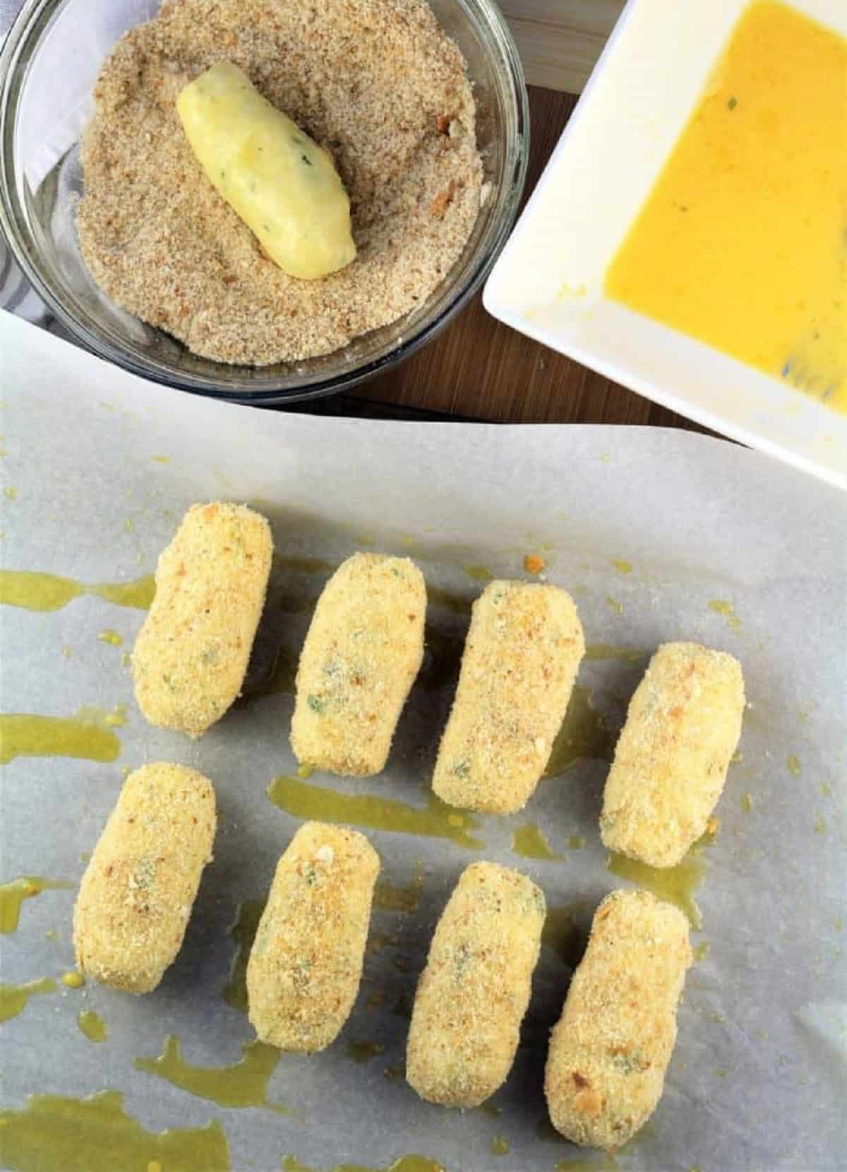 Dredging potato croquettes in egg wash and breadcrumbs.