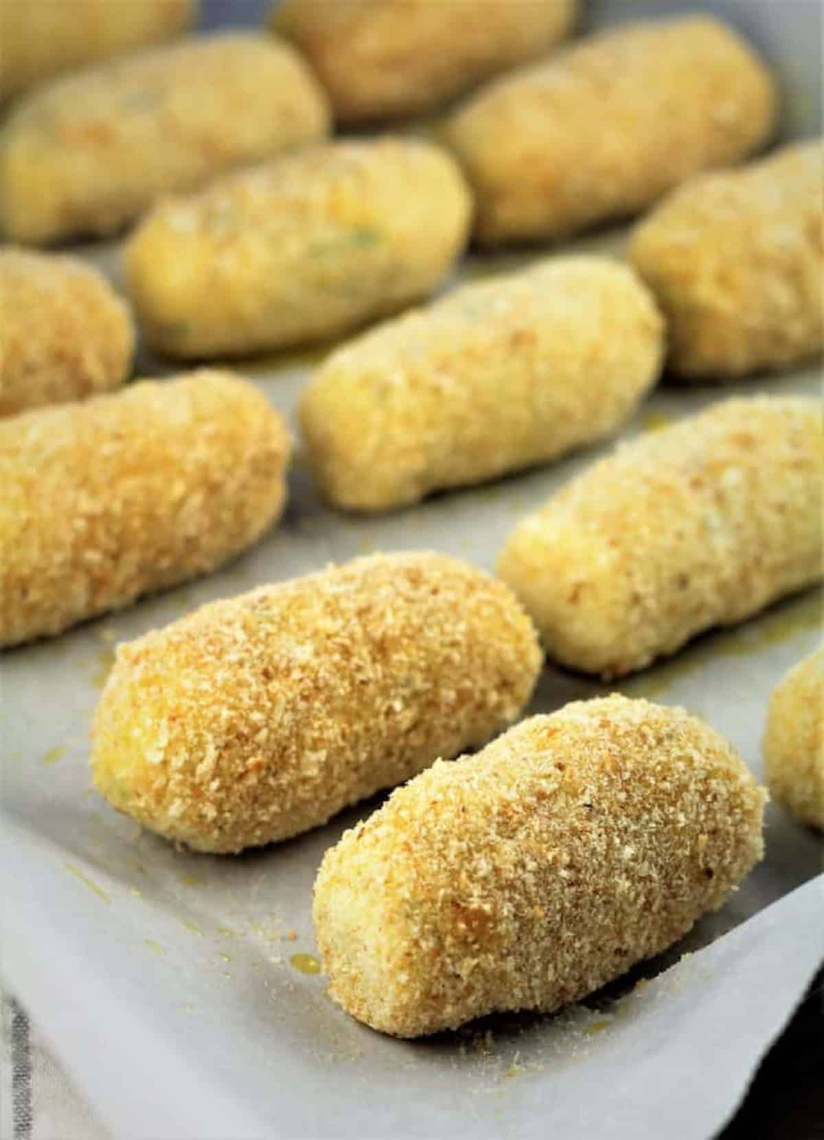 Breaded potato croquettes on baking sheet. 
