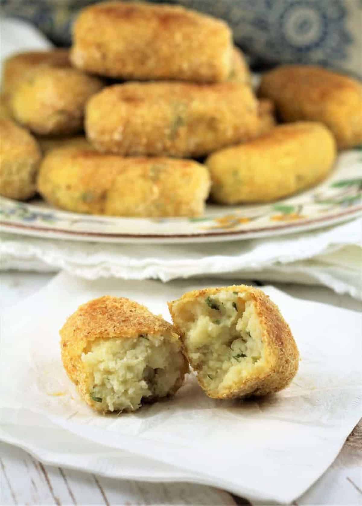 Mashed potato croquette (cazzilli Siciliani) cut open on napkin with full plate of croquettes behind it.