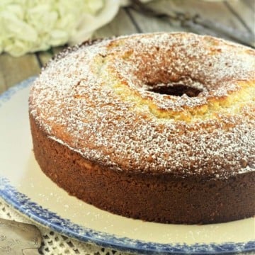 orange bundt cake on blue rimmed plate with cake spatula and flowers and orange in background