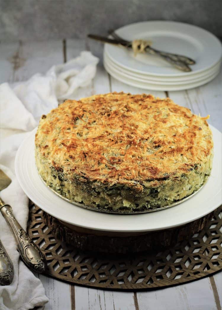 potato and spinach gateau on white plate with plates and utensils in background