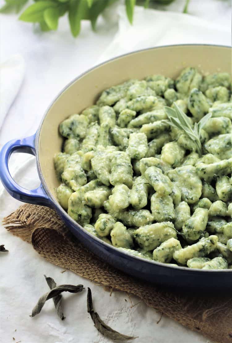 blue skillet filled with spinach gnocchi with butter sage sauce