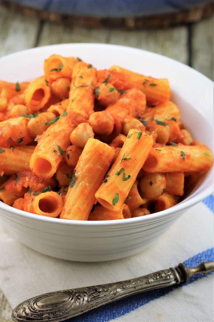 close up of white bowl with pasta with chickpeas in tomato sauce
