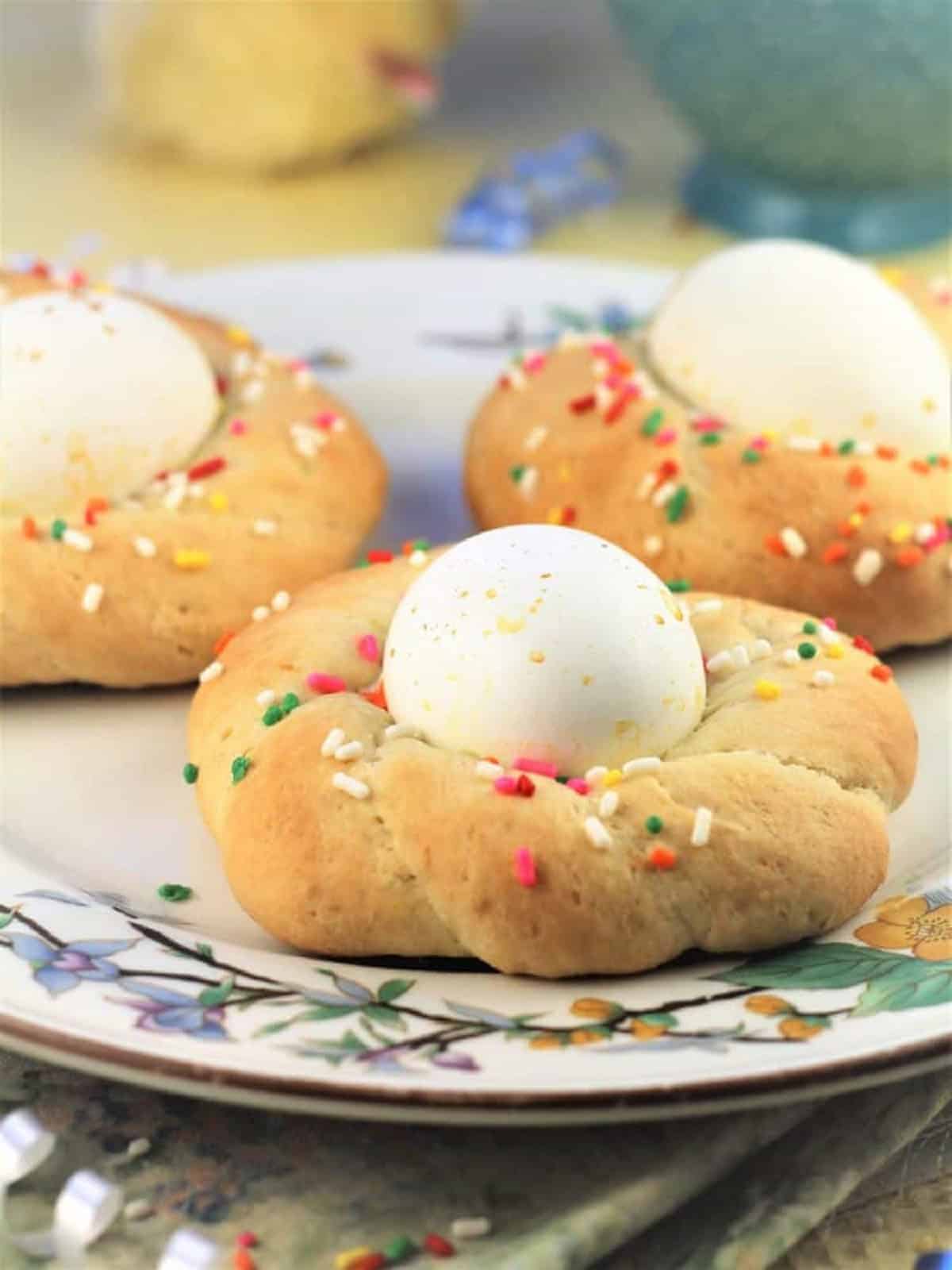 Sicilian Easter Cookies with Eggs Sicilian Easter cookies with eggs in the center covered with sprinkles on plate.