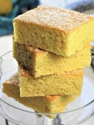 Lemon vanilla snack cake squares piled on glass plate.