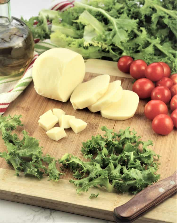 wood board filled with escarole, cheese, cherry tomatoes with knife on side