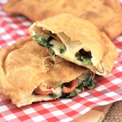 Pitoni Messinesi (Sicilian Fried Calzone) cut in half to reveal filling on red and white checked paper