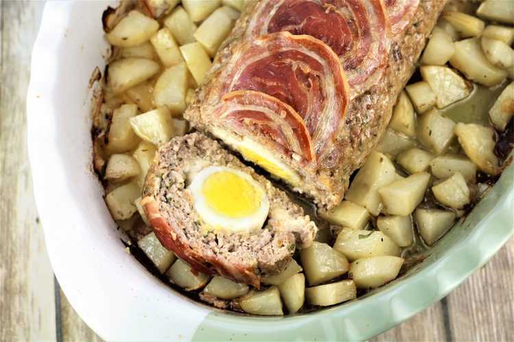 overhead view of polpettone with hard boiled eggs in casserole dish surrounded by roast potatoes