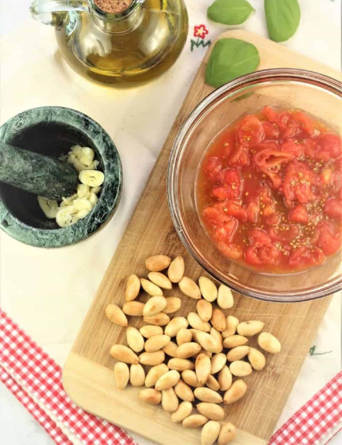 Chopeed blanched cherry tomatoes in bowl, peeled almonds, mortar and pestle with garlic and olive oil.