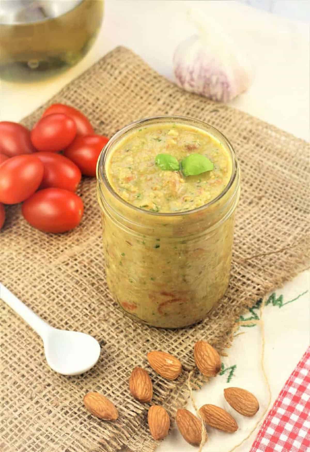 Pesto alla Trapanese in glass jar surrounde dby almonds, cherry tomatoes, garlic and olive oil.