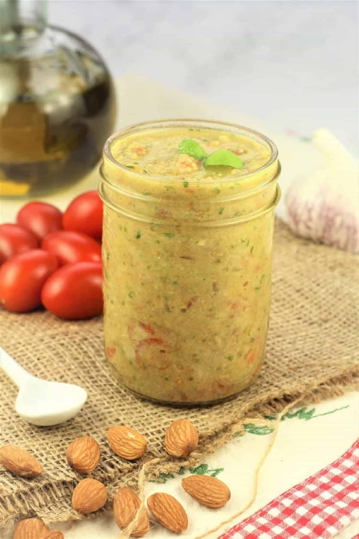 Pesto alla Trapanese (Sicilian Pesto) Sicilian pesto alla Trapanese in glass jar surrounded by almonds, cherry tomatoes, garlic bulb and olive oil.