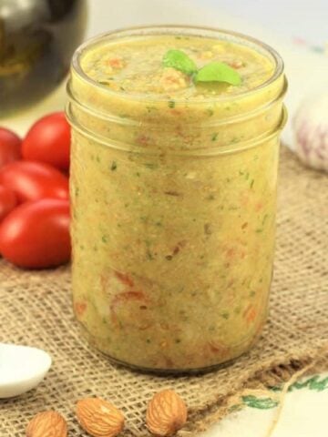 Sicilian pesto alla Trapanese in glass jar surrounded by cherry tomatoes, garlic and olive oil.