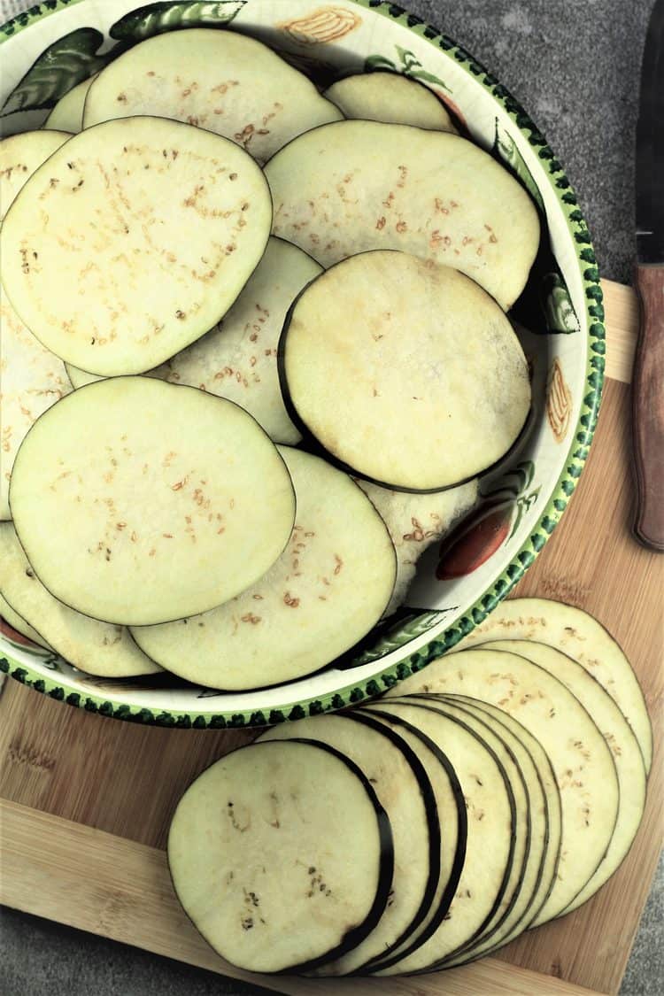 eggplant rounds in large bowl with sliced eggplant on side on wood board