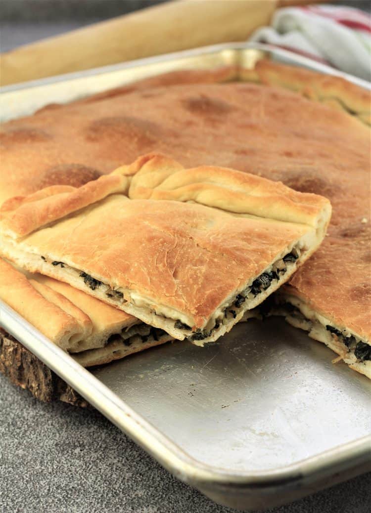 square of swiss chard filled pizza sitting on whole pizza on baking sheet