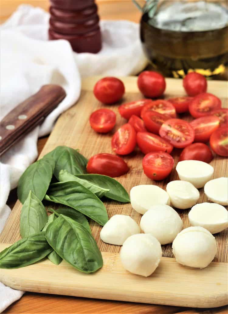 wood board with halved cherry tomatoes, mozzarella balls and basil leaves