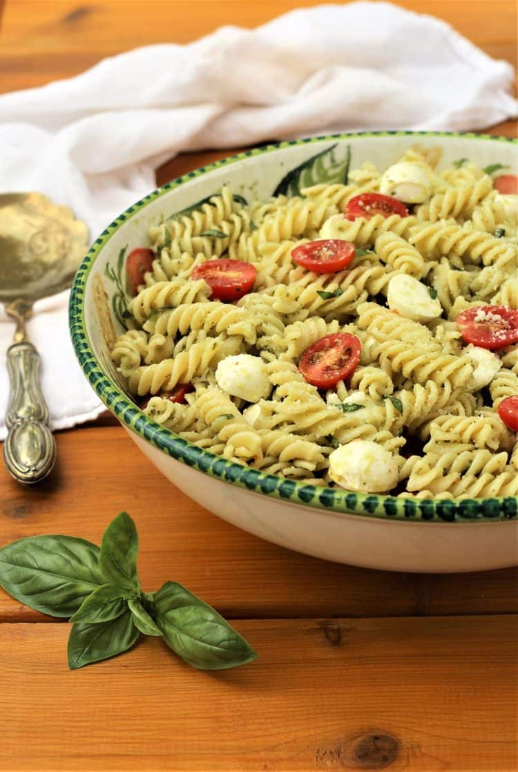 large bowl filled with Caprese Pasta Salad with Pesto on wood table with basil leaves in forefront