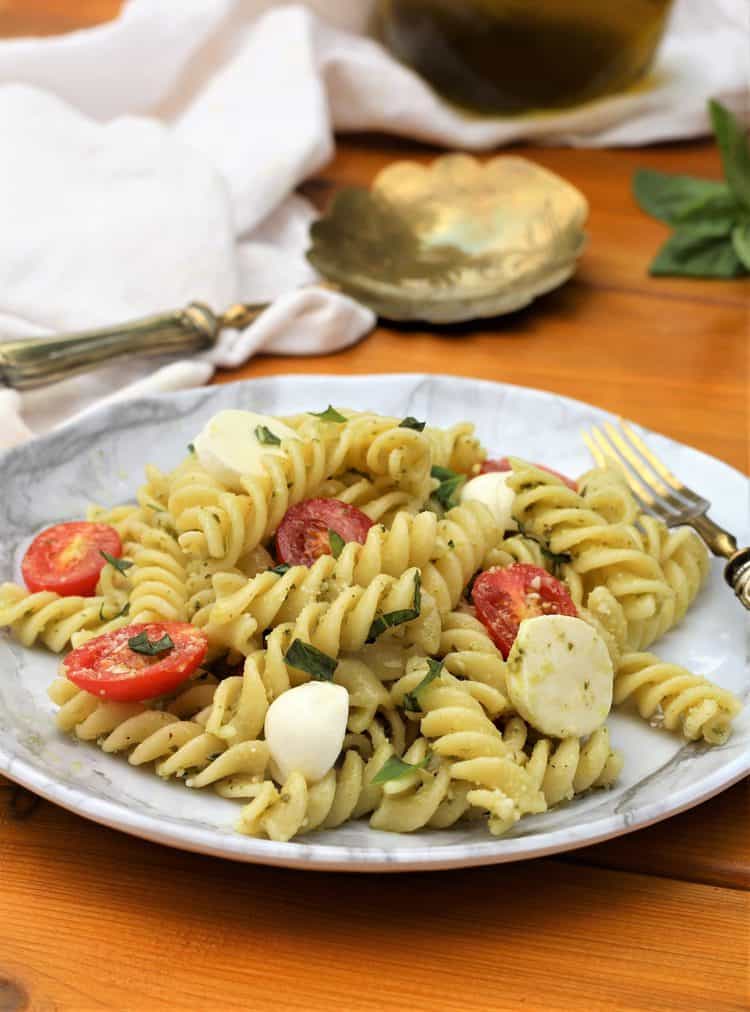 white plate filled with Caprese Pasta Salad with Pesto on wood table