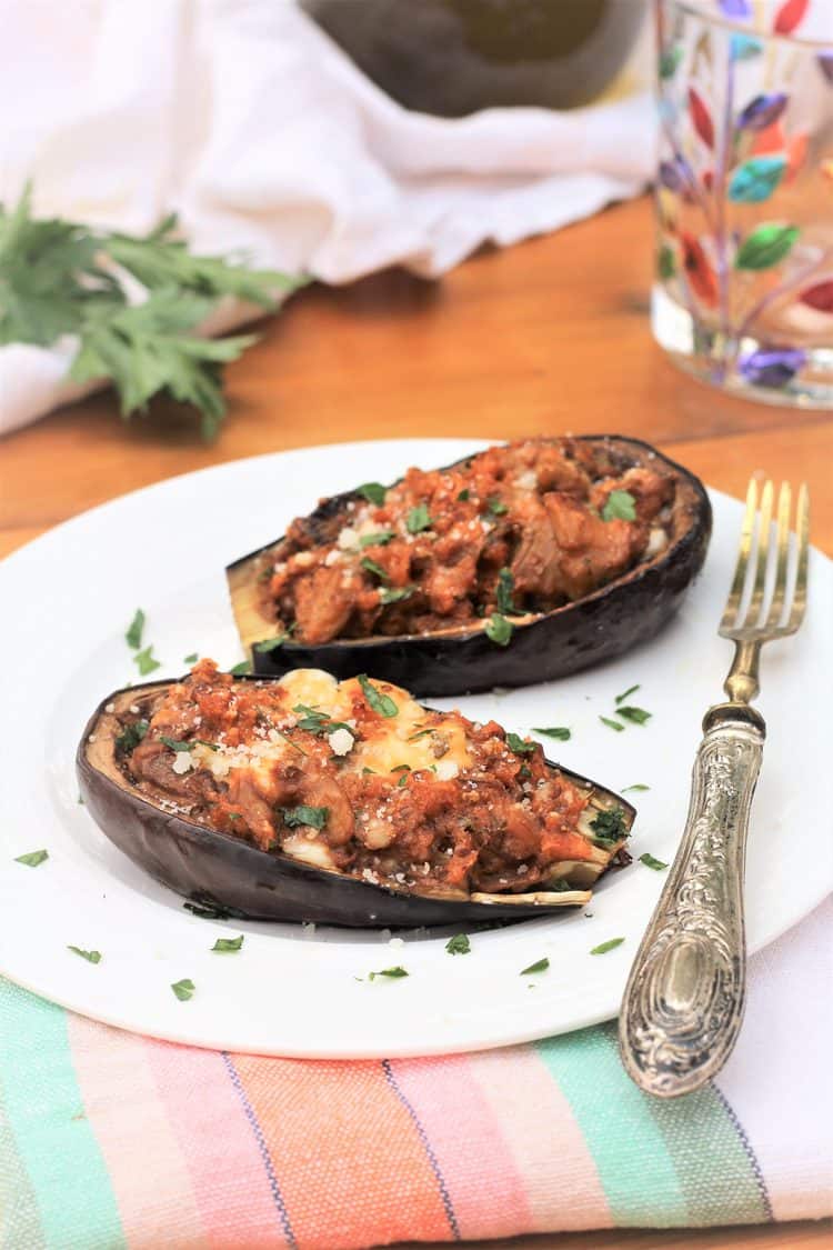Stuffed baby eggplant halves on white plate with silver fork on side
