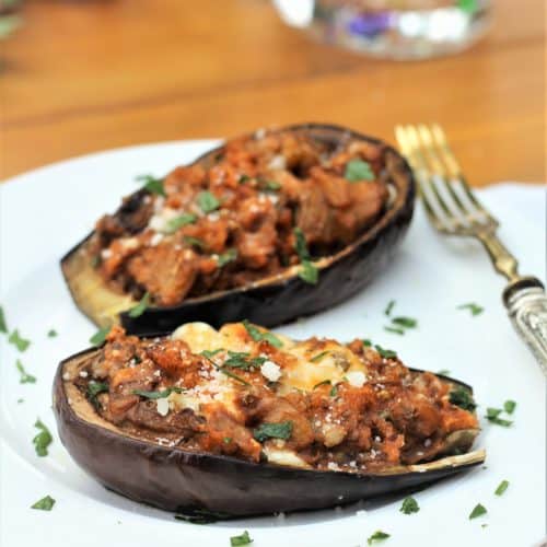 stuffed baby eggplant halves on white plate with silver fork on side