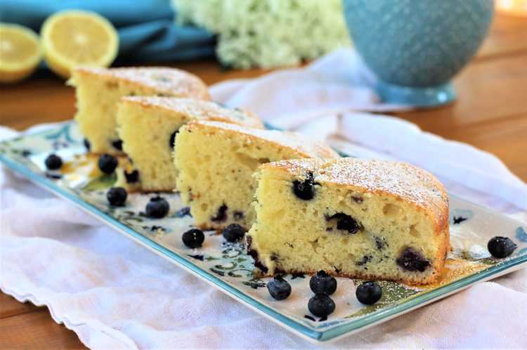 3 slices of Blueberry Olive Oil Cake on rectangular serving plate with lemon wedges in background