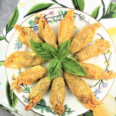 overhead view of baked zucchini blossoms on round flowery plate with basil leaves in center