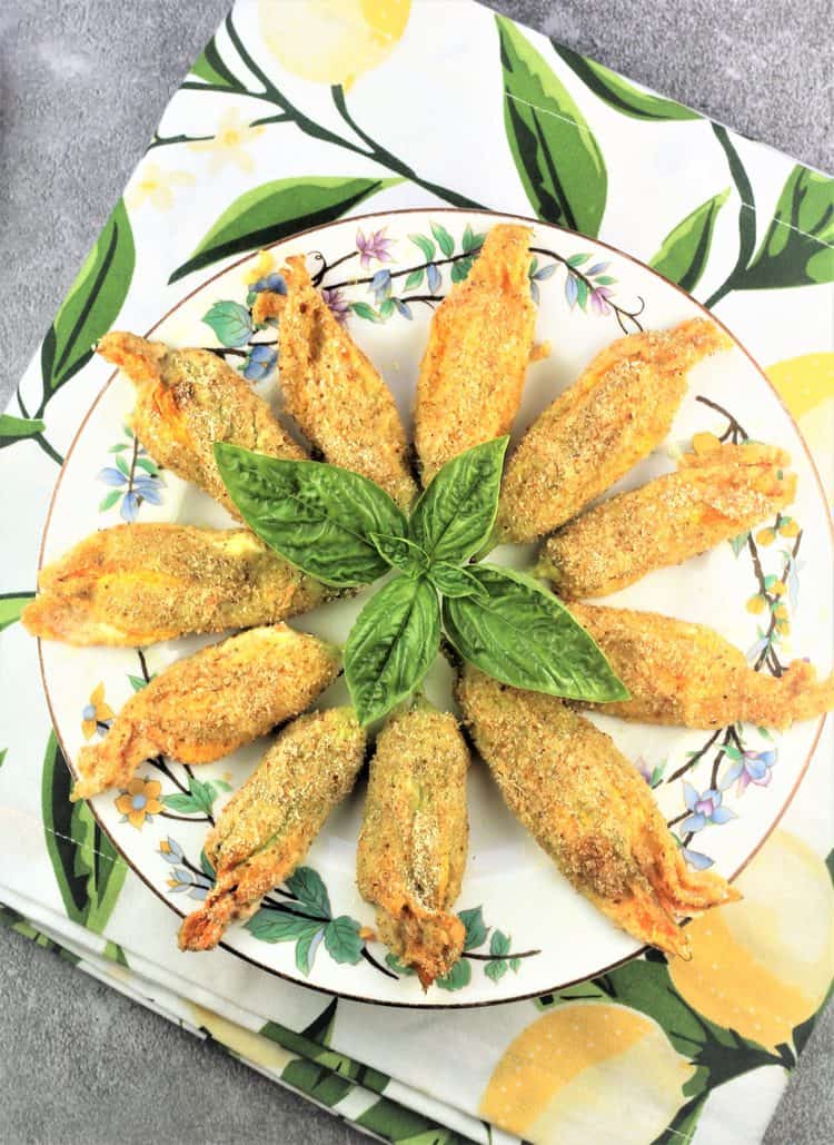 baked stuffed zucchini blossoms fanned out on flowery plate with basil leaves in center
