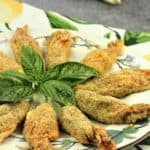baked stuffed zucchini blossoms on round plate with basil leaves in center