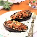 Stuffed baby eggplant halves with breadcrumbs and cheese on plate with fork.