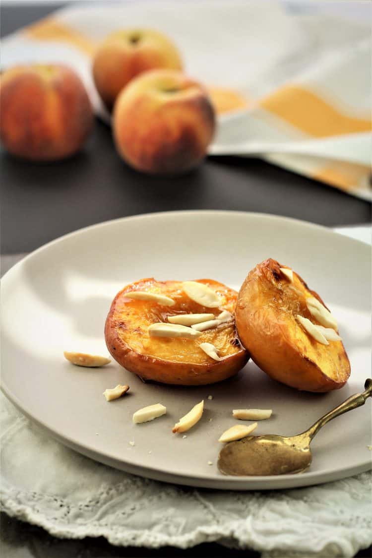 2 maple roasted peach halves topped with slivered almonds on plate with spoon