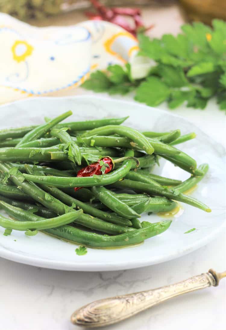 Italian green bean salad on white plate with parsley in background