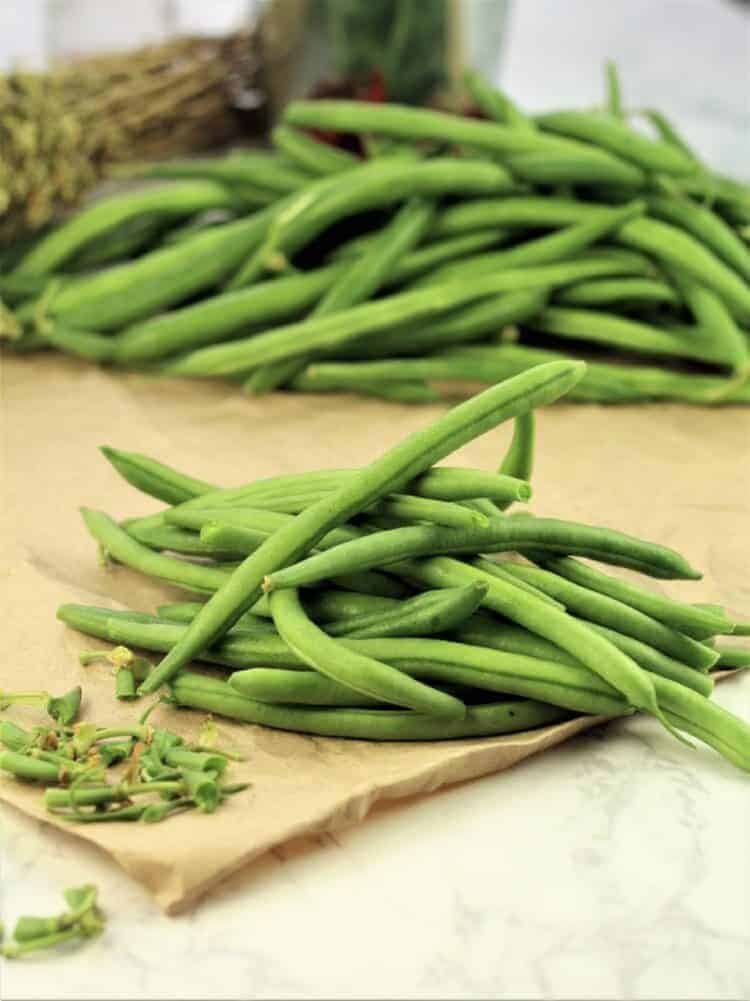 Green beans with ends trimmed piled on wood board.