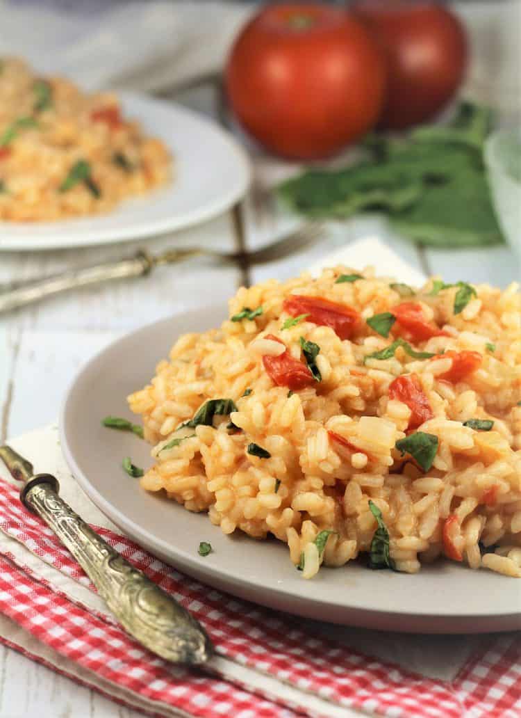 plate with tomato and basil risotto on red checkered dish cloth with tomatoes in background