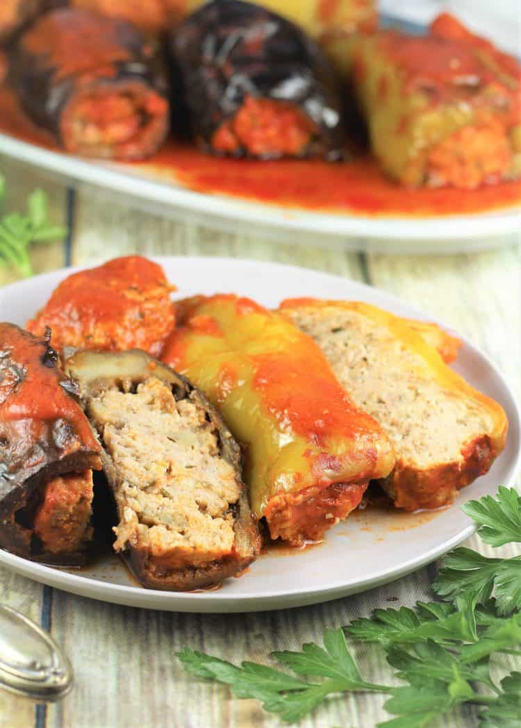 stuffed eggplant and pepper sliced in half on plate with serving platter behind it