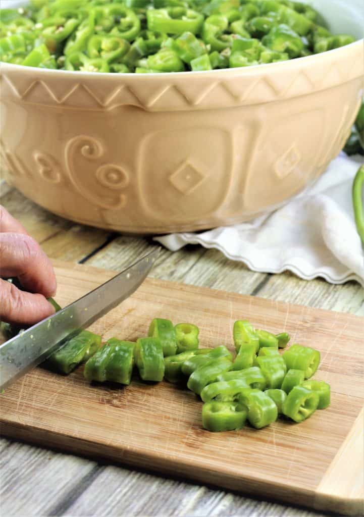 cutting green peppers into rounds on cutting board with large bowl full in background