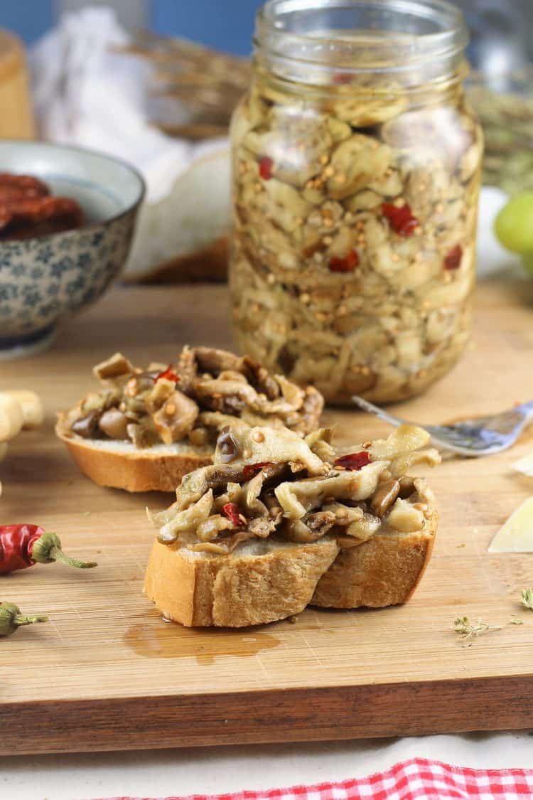 pickled eggplant crostini on wood board with jar behind them