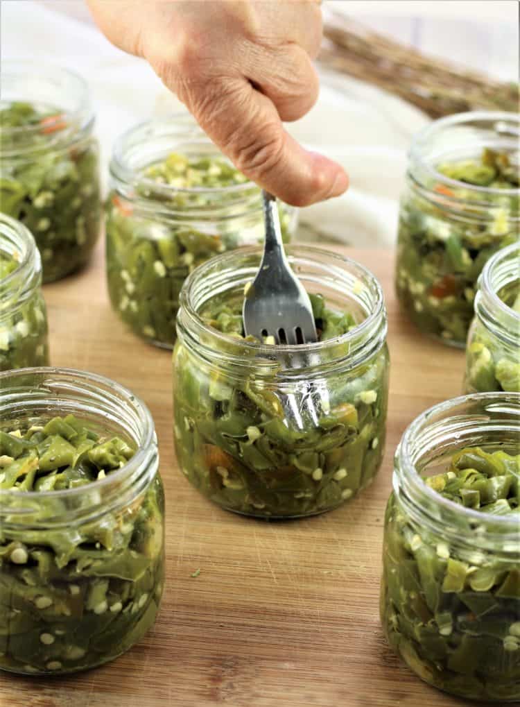 packing hot pickled peppers in jars with fork
