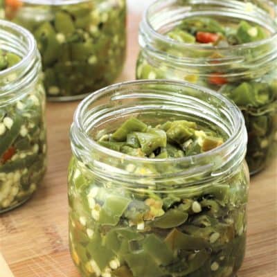 jars of green pickled hot peppers on wood board