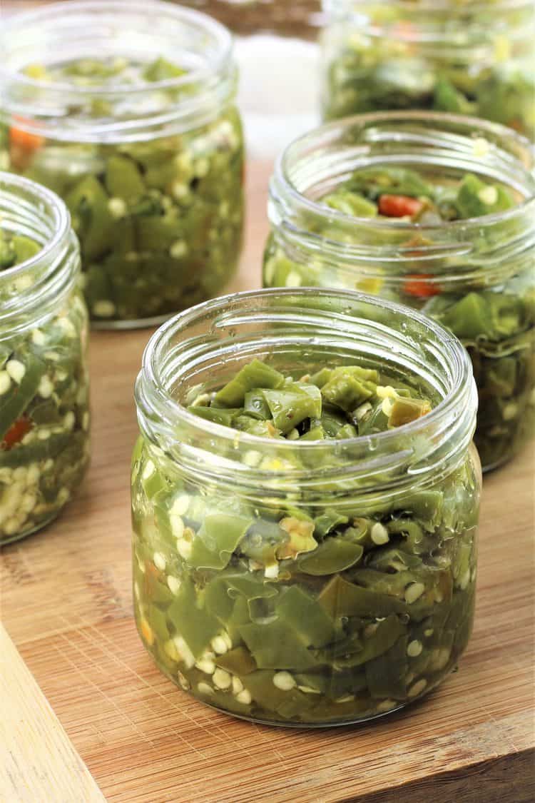 jars of hot pickled green peppers on a wood board