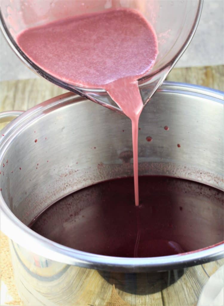 pouring cornstarch grape must mixture into pot with grape must in it