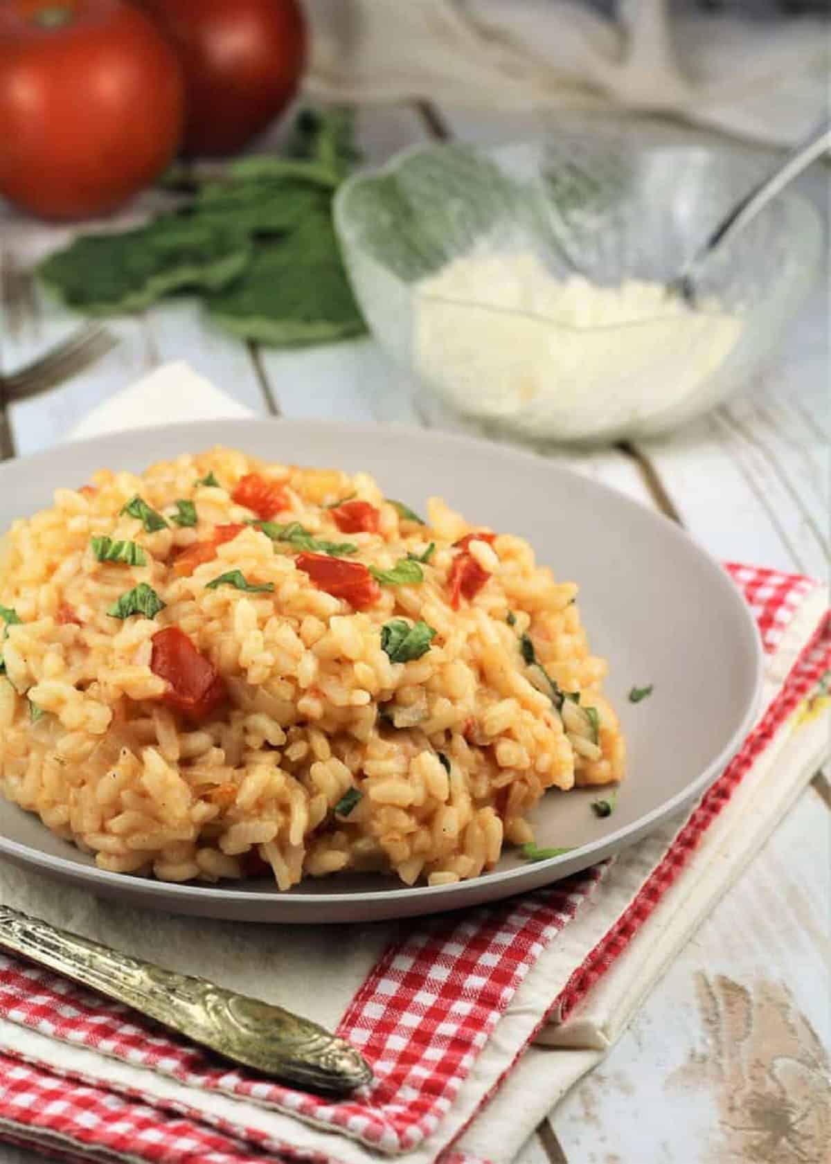 Tomato basil risotto in plate next to bowl of grated parmigiano cheese.