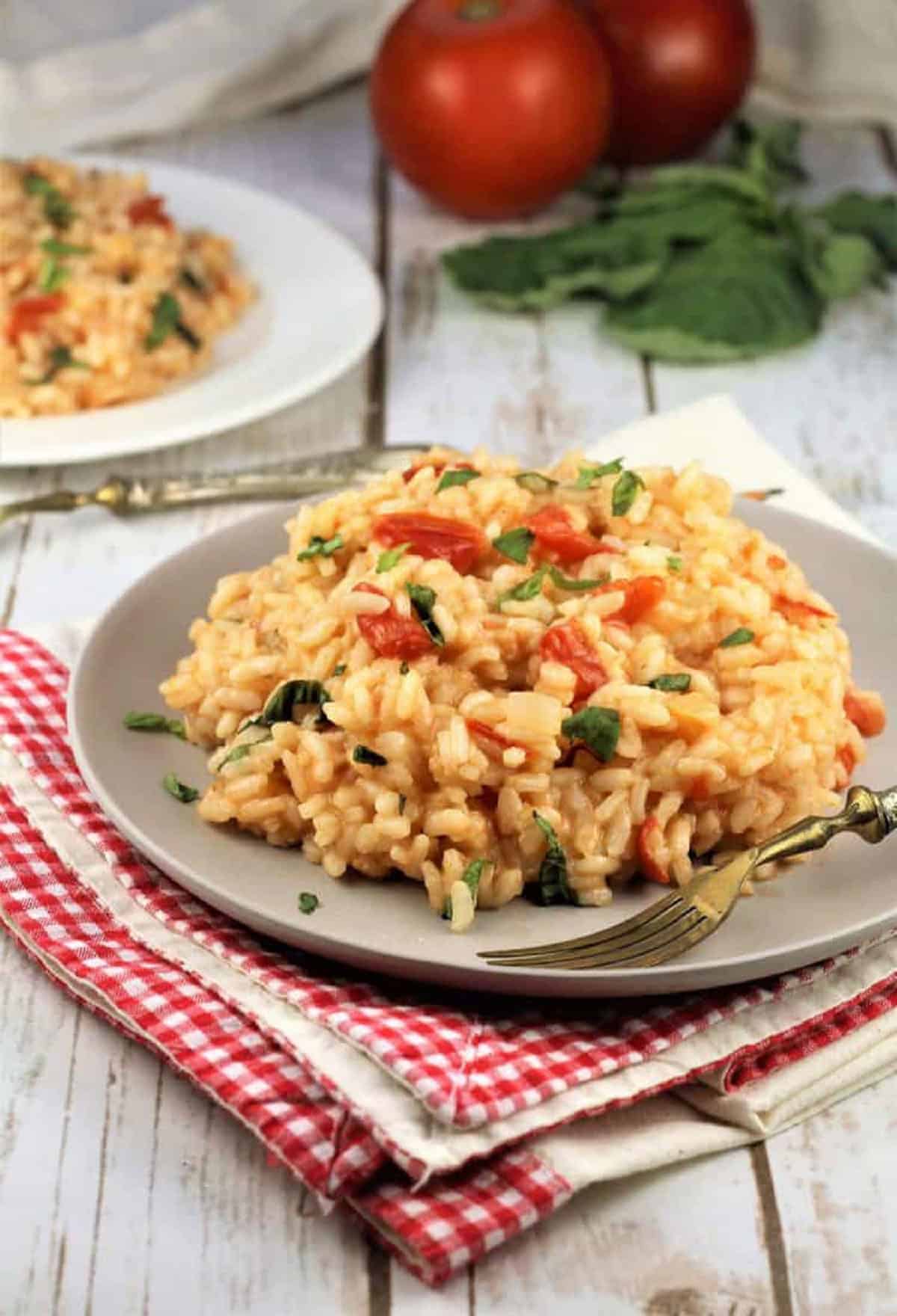 Tomato basil risotto plated with basil leaves and tomatoes next to it.