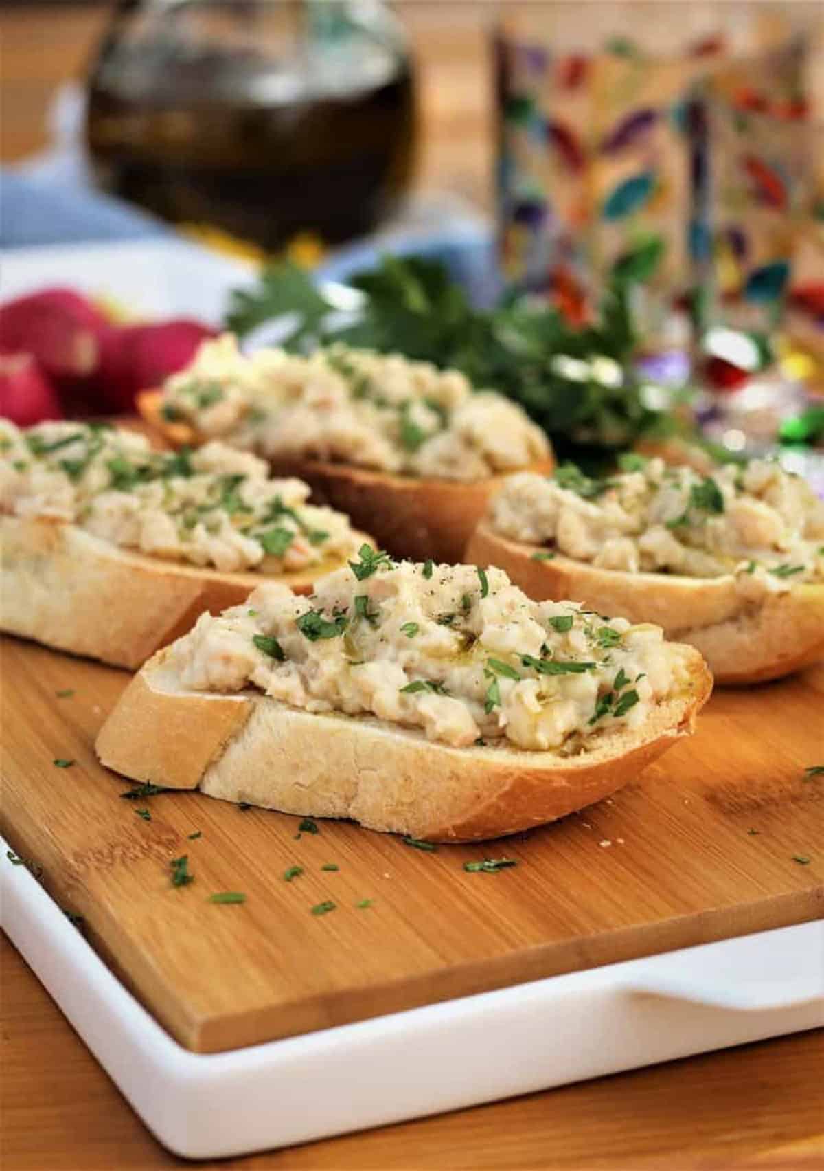 White Bean Dip White bean crostini served on wood board.