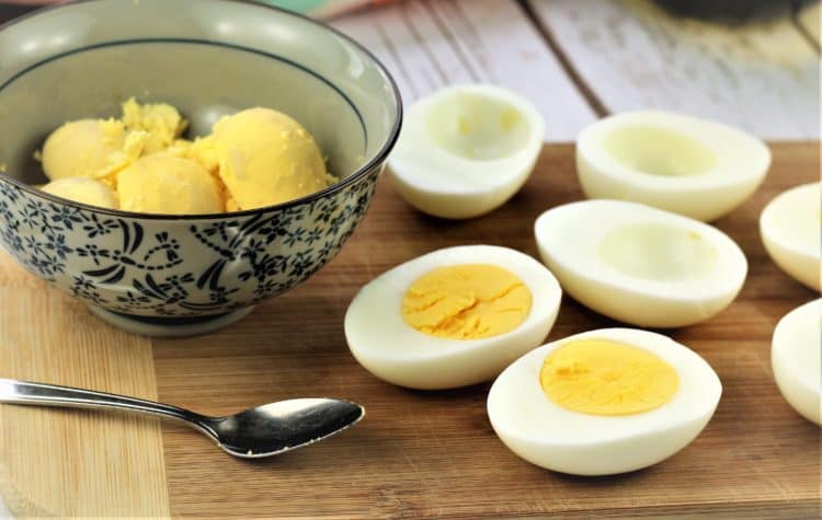 scooping out egg yolks from halved hard boiled eggs into bowl