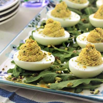 deviled eggs on platter with arugula and chopped pistachios