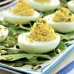 deviled eggs on platter covered with arugula and chopped pistachios